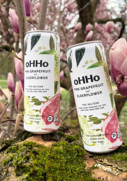 Cans of oHHo Pink Grapefruit and Elderflower seltzer with flowers in the background.